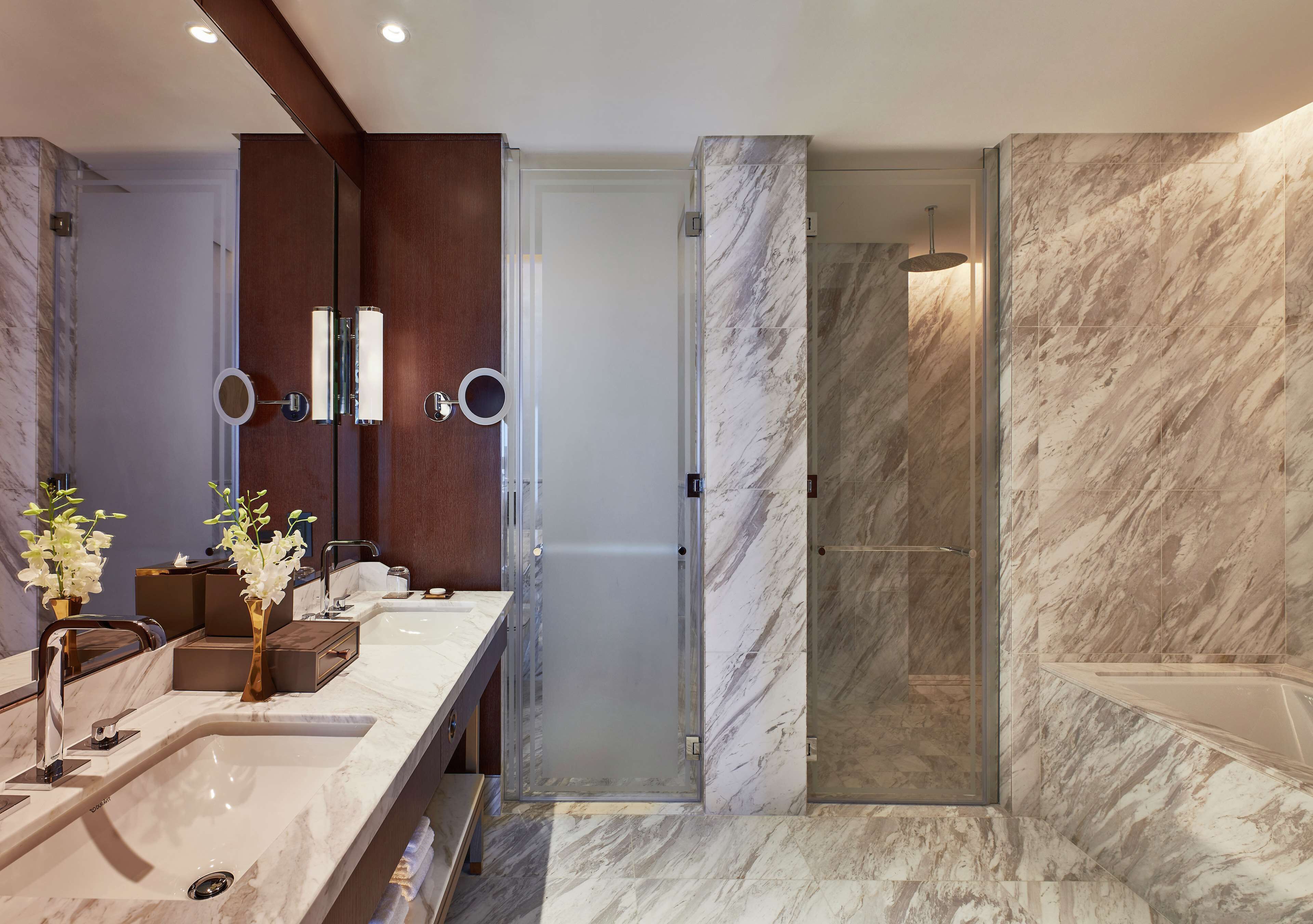 A modern bathroom with a marble sink, a glass shower enclosure, and a large mirror.