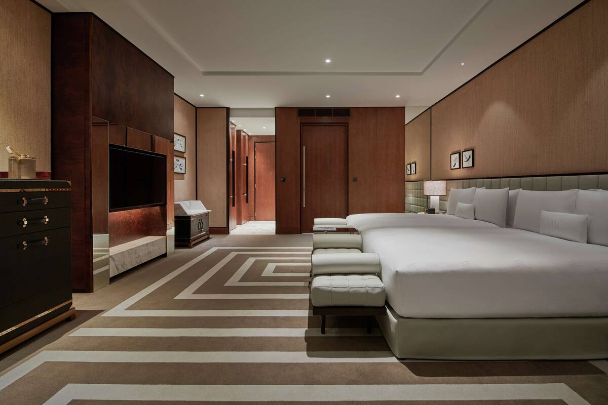 A modern hotel room with a large bed, a TV, a dresser, and a walk-in closet.