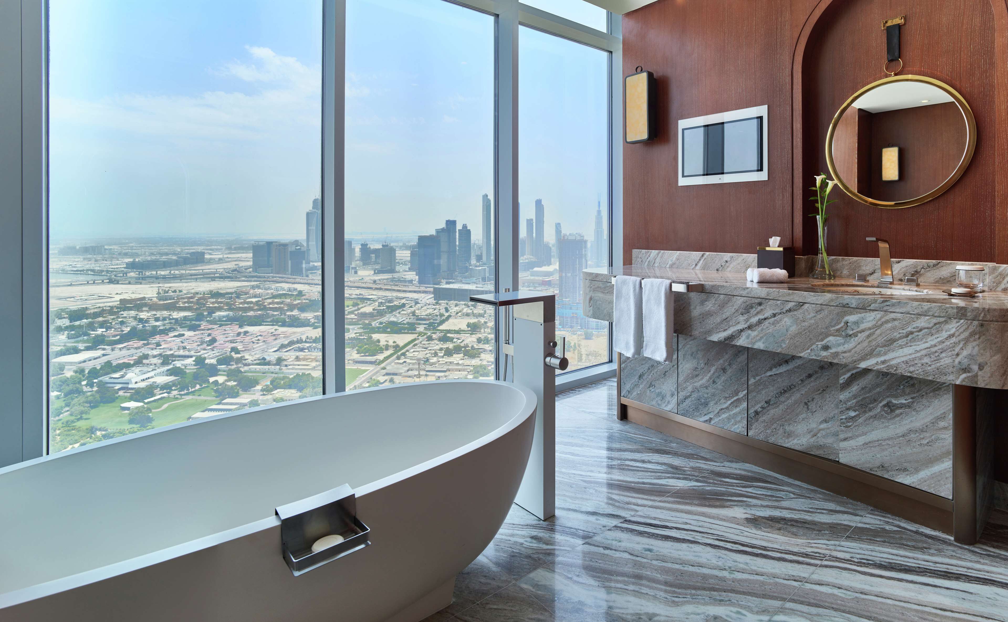 Une salle de bain moderne avec une baignoire sur pieds, un meuble-lavabo en marbre, un grand miroir et une vue sur la ville.