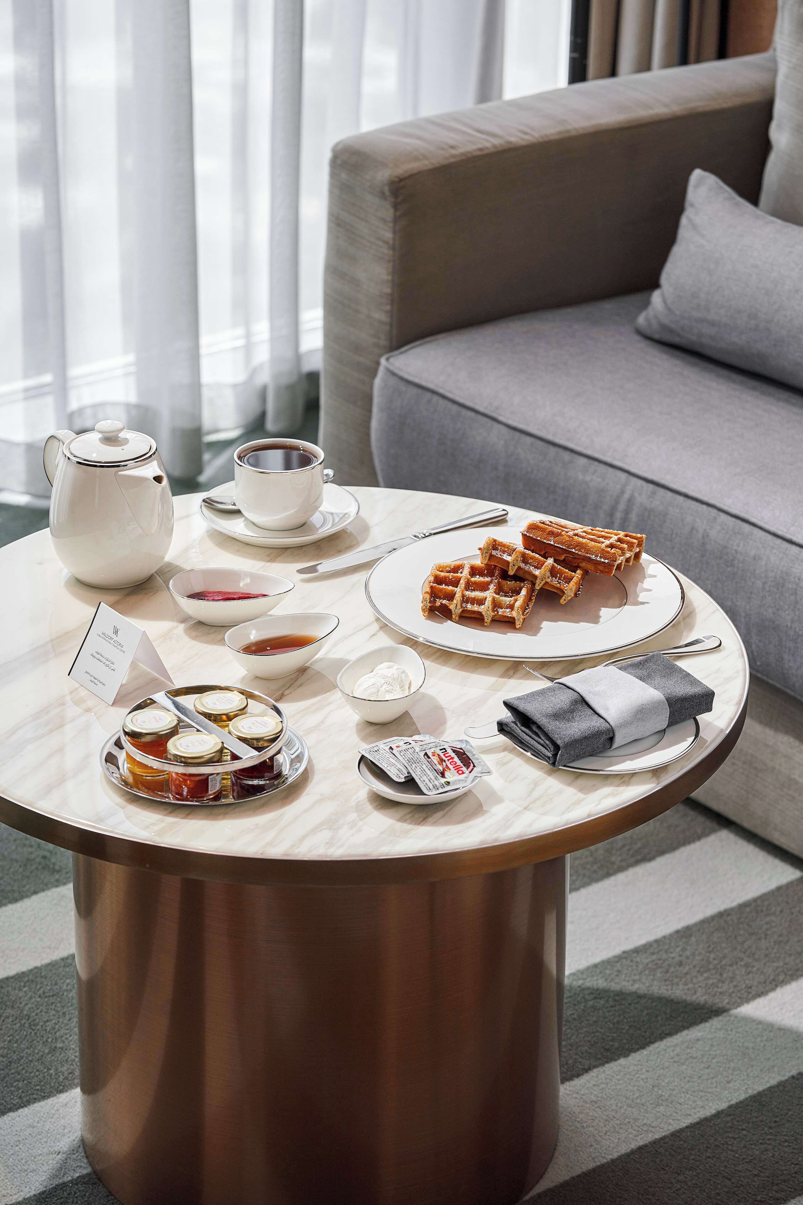 Ein runder Tisch mit einem weißen Teekessel, Tassen, Waffeln und einer Marmeladenschale.