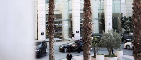 A modern building with a glass facade, palm trees, and a circular plaza with potted plants.