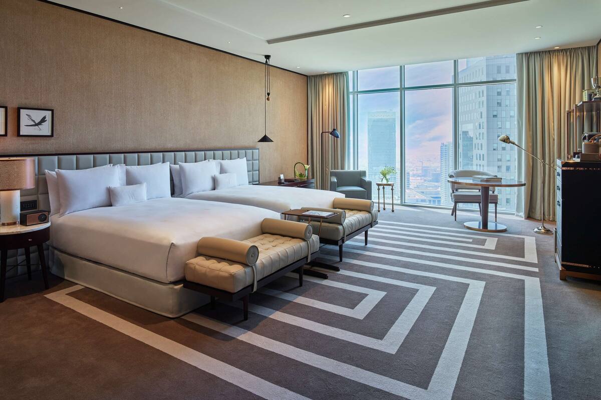 A modern hotel room with two beds, a sofa, a TV, and a city view.