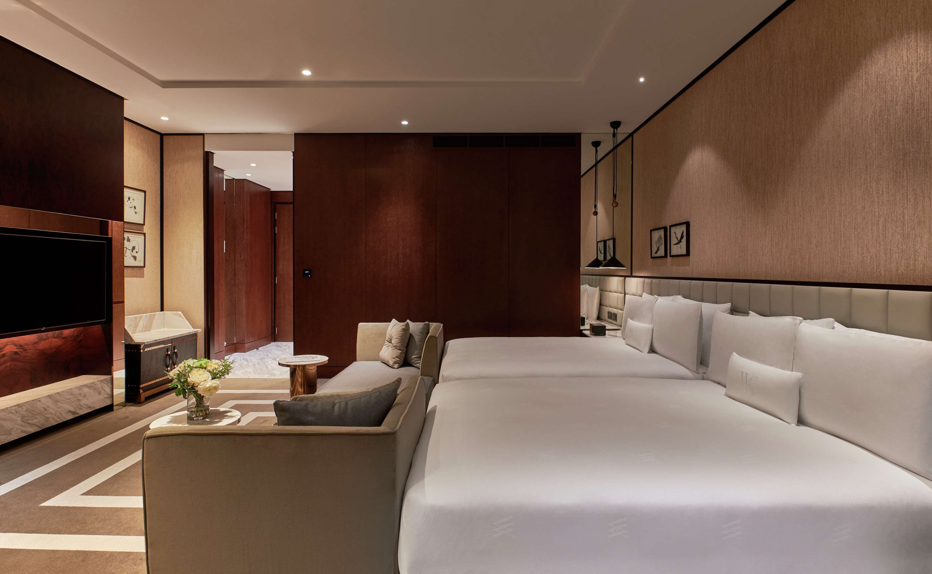 Una habitación de hotel moderna con una cama grande, un sofá, un televisor y una mesita con flores.