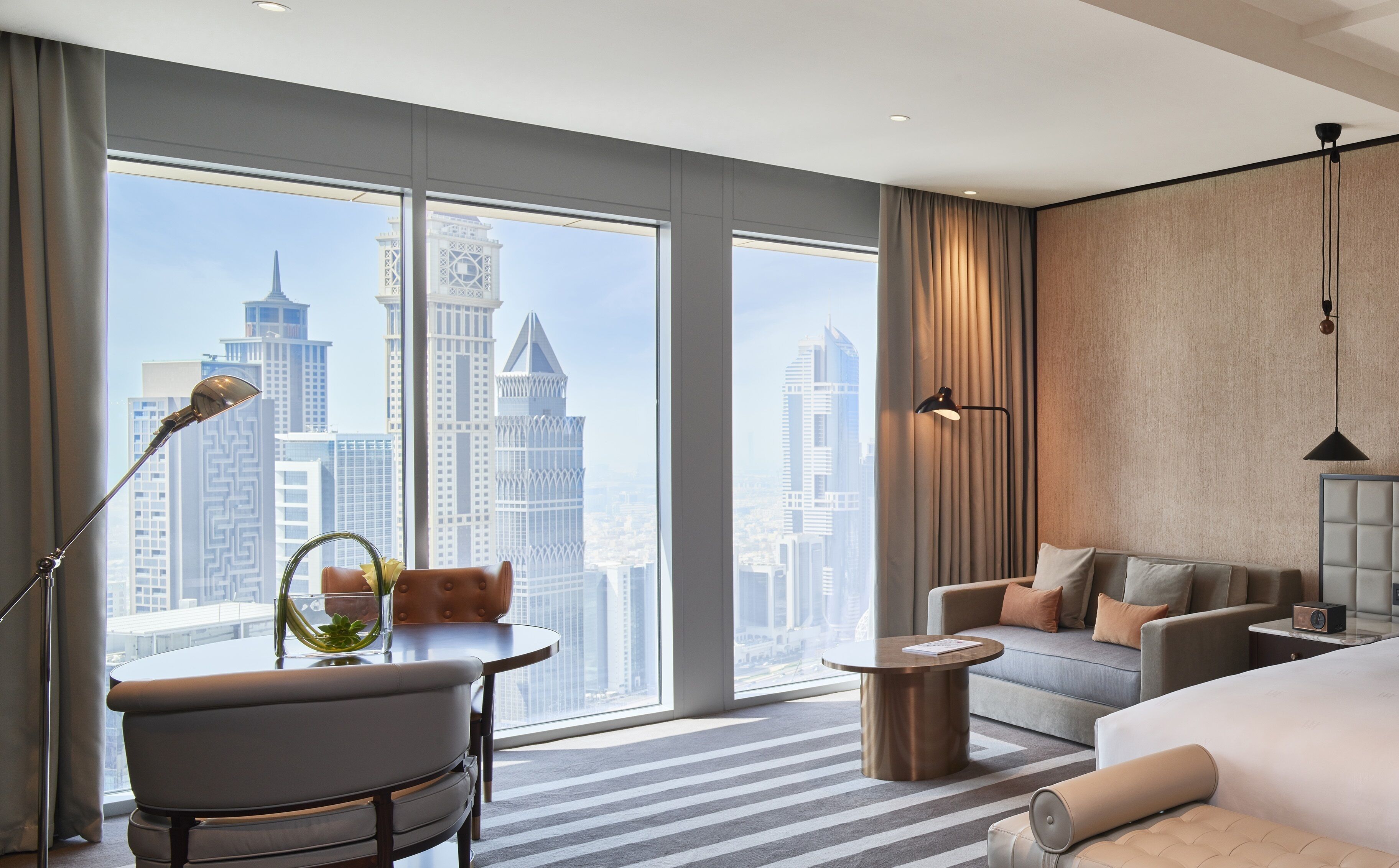 Een moderne hotelkamer met een groot raam met uitzicht op de stad, een bank, een klein tafeltje en een bed.