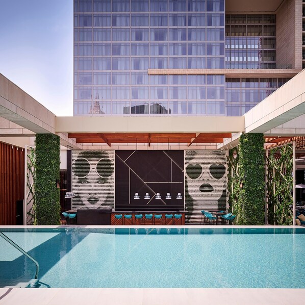 Un hotel moderno con piscina, asientos al aire libre y un edificio grande al fondo.