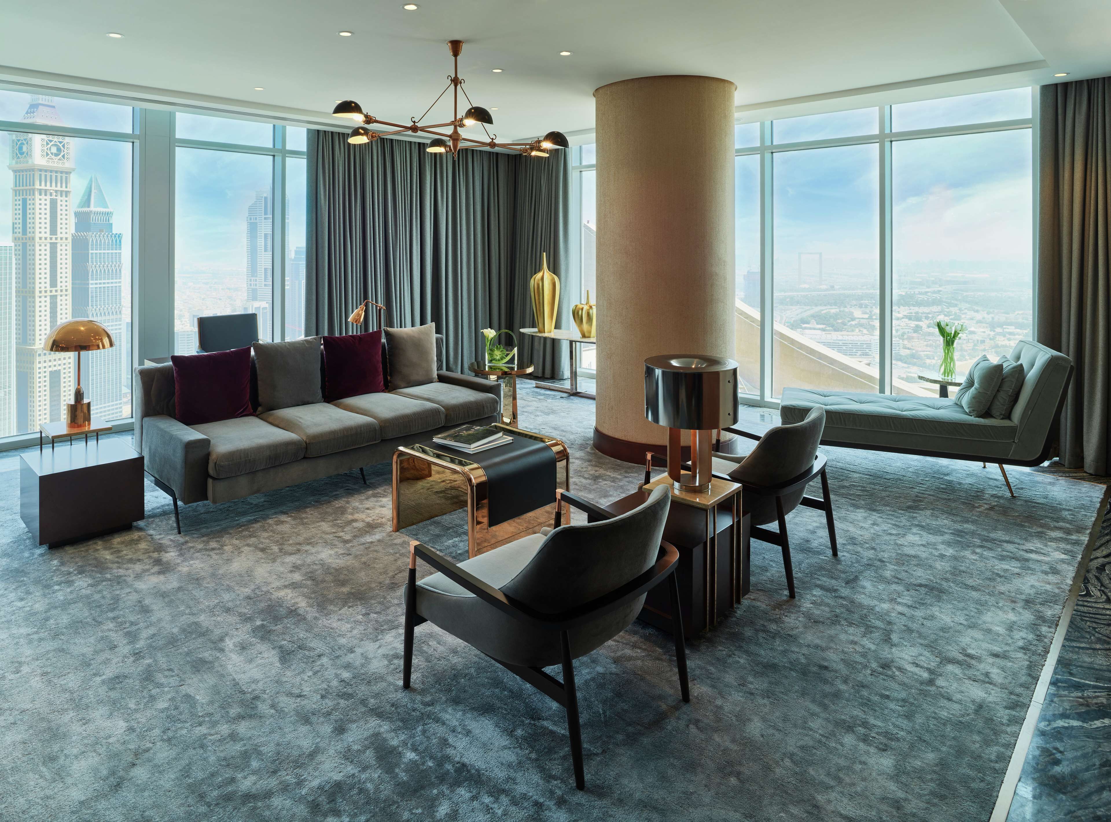 Uma sala de estar moderna com sofá, poltronas, mesa de centro e uma grande janela com vista para a cidade.