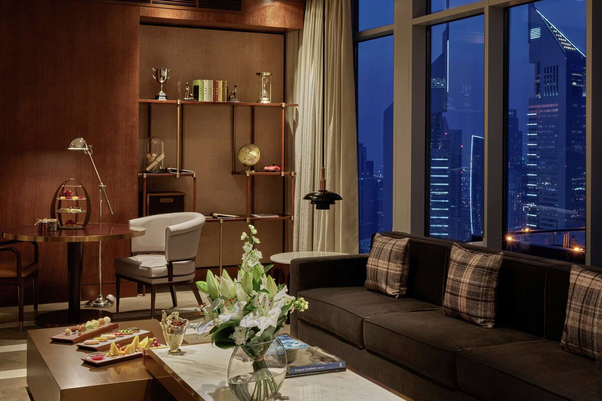 A modern living room with a city view, a bookshelf, a dining table with desserts, and a sofa with plaid cushions.