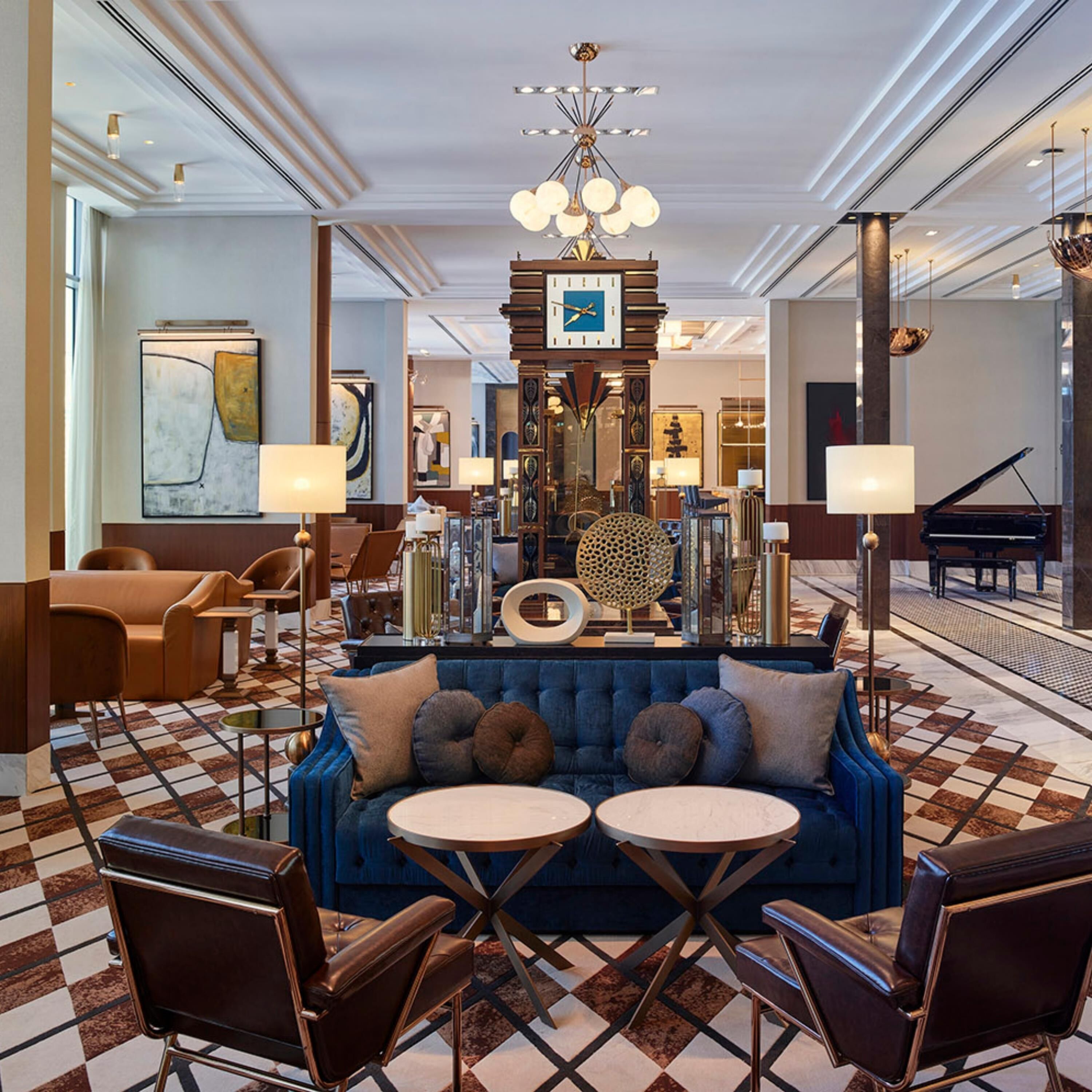A spacious lobby with a blue sofa, two round tables, and a grand piano.