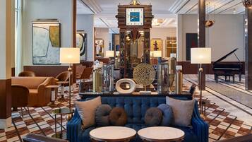 A spacious lobby with a blue sofa, two round tables, and a grand piano.