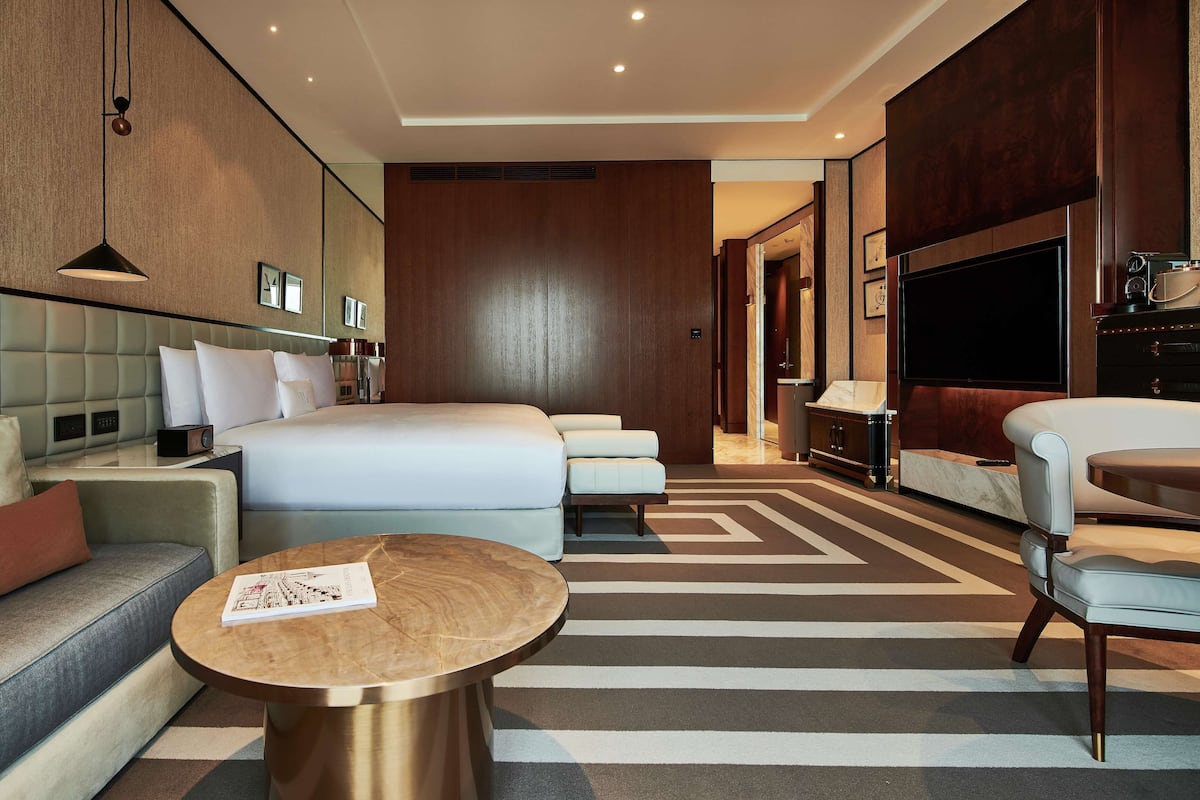 A modern hotel room with a large bed, a sofa, a coffee table, and a TV.