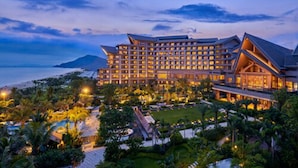 Un hotel grande con varios pisos, un jardín cuidado y vista al océano.