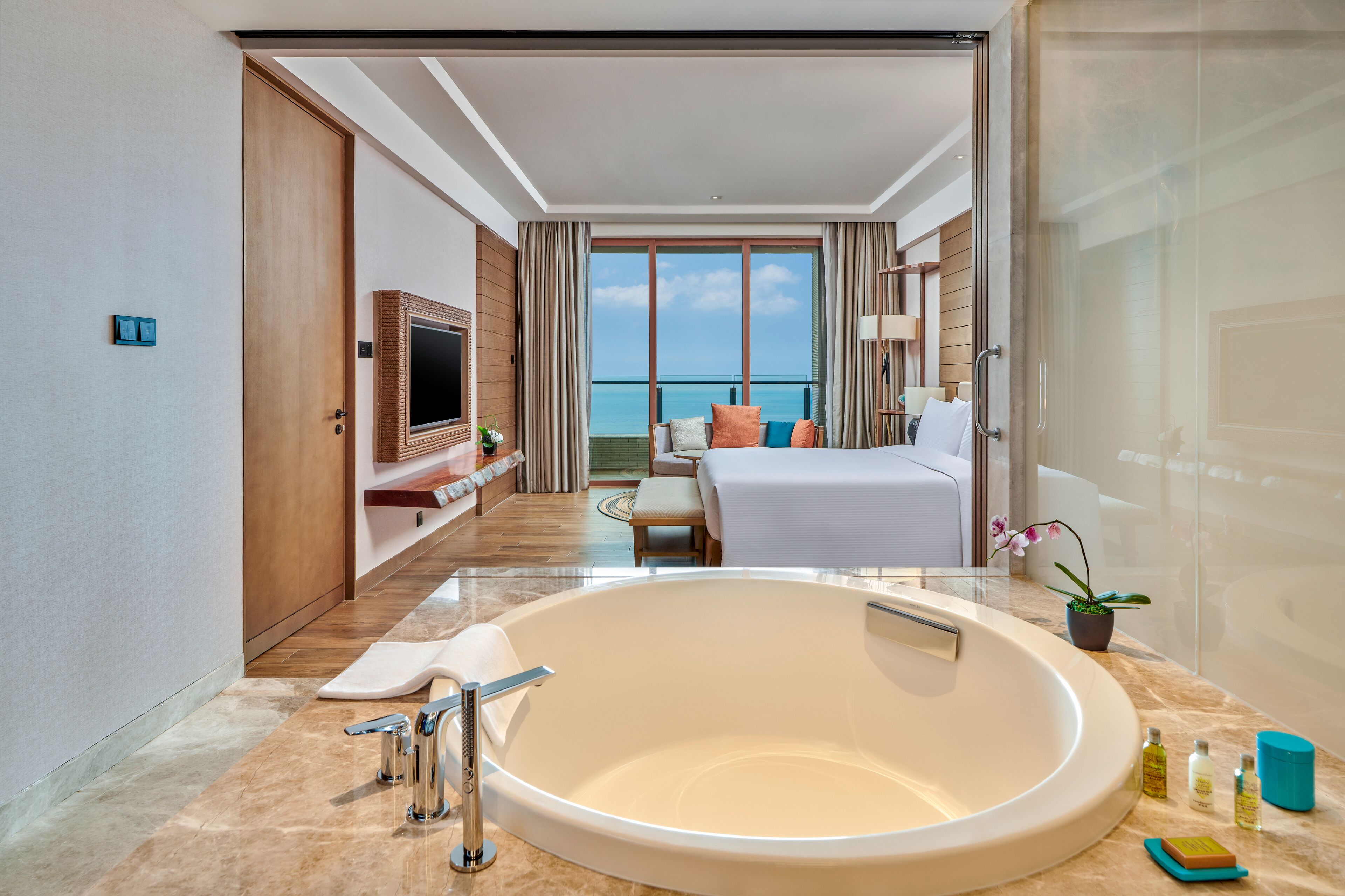 Una habitación de hotel moderna con una bañera grande, una cama, un televisor y vistas al océano.