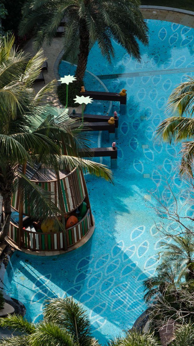 Ein Pool mit rundem Sonnendeck, Palmen und einer kleinen Spielbereitschaft mit einer Rutsche.