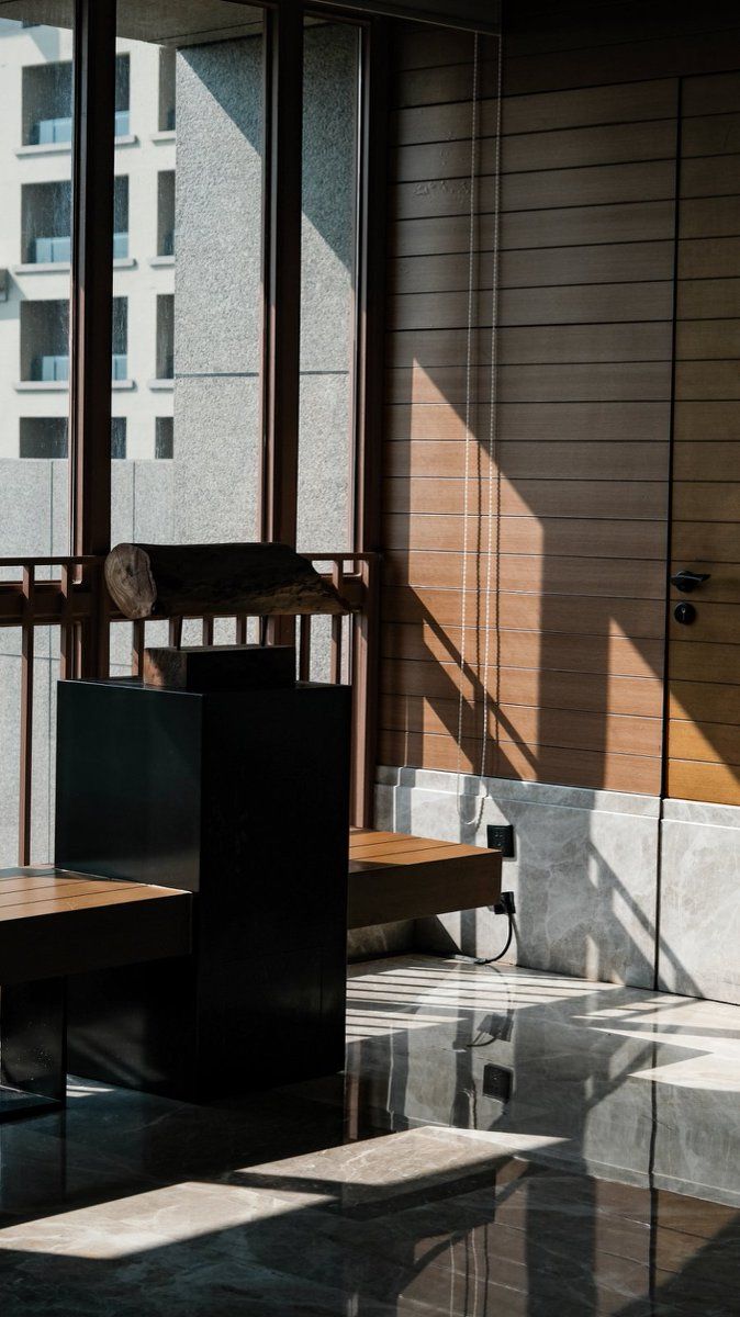 Um interior moderno com um banco de madeira, uma mesa e vista para um edifício através de uma janela.