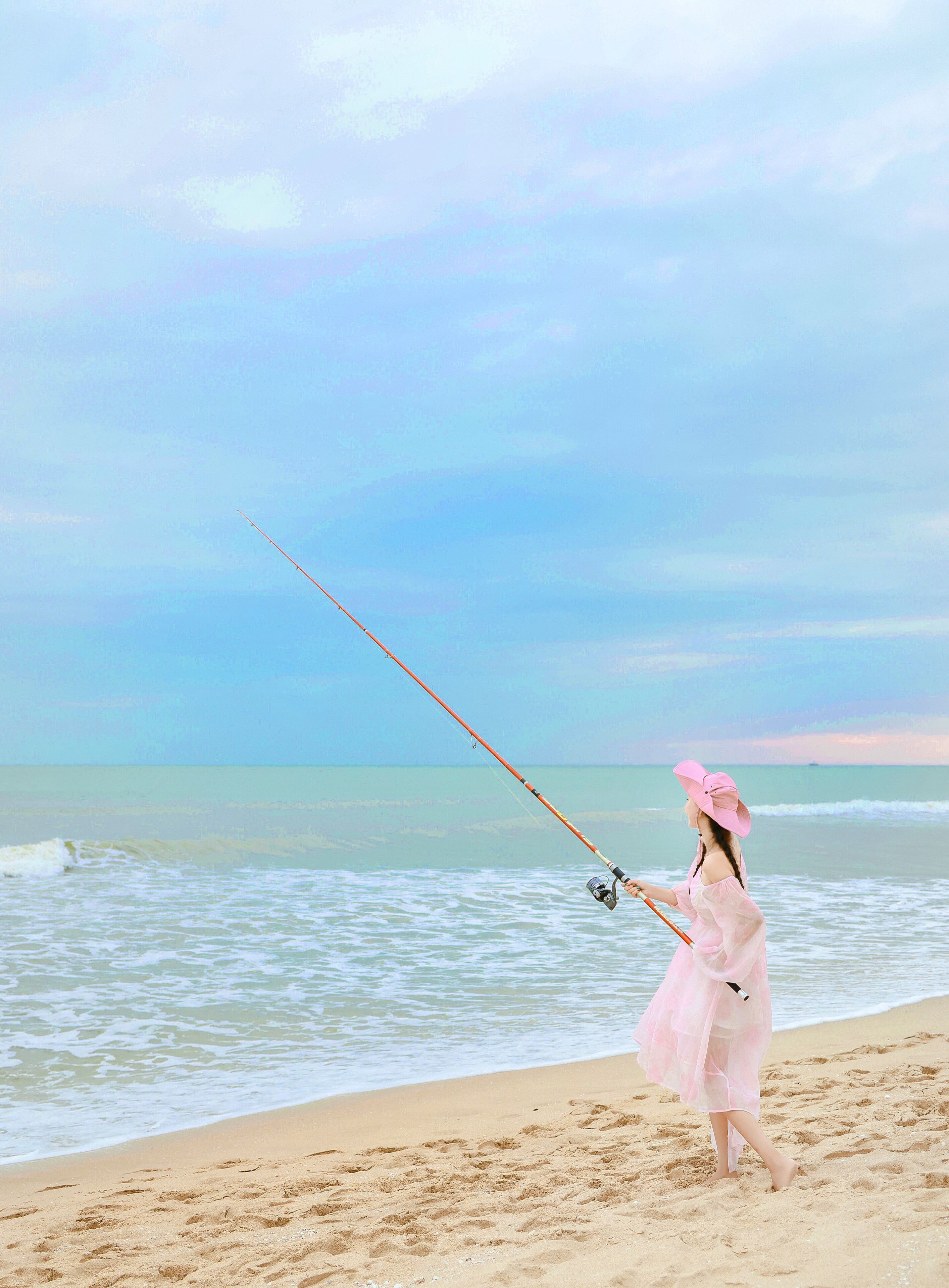 A person fishing on a beach with a clear sky.