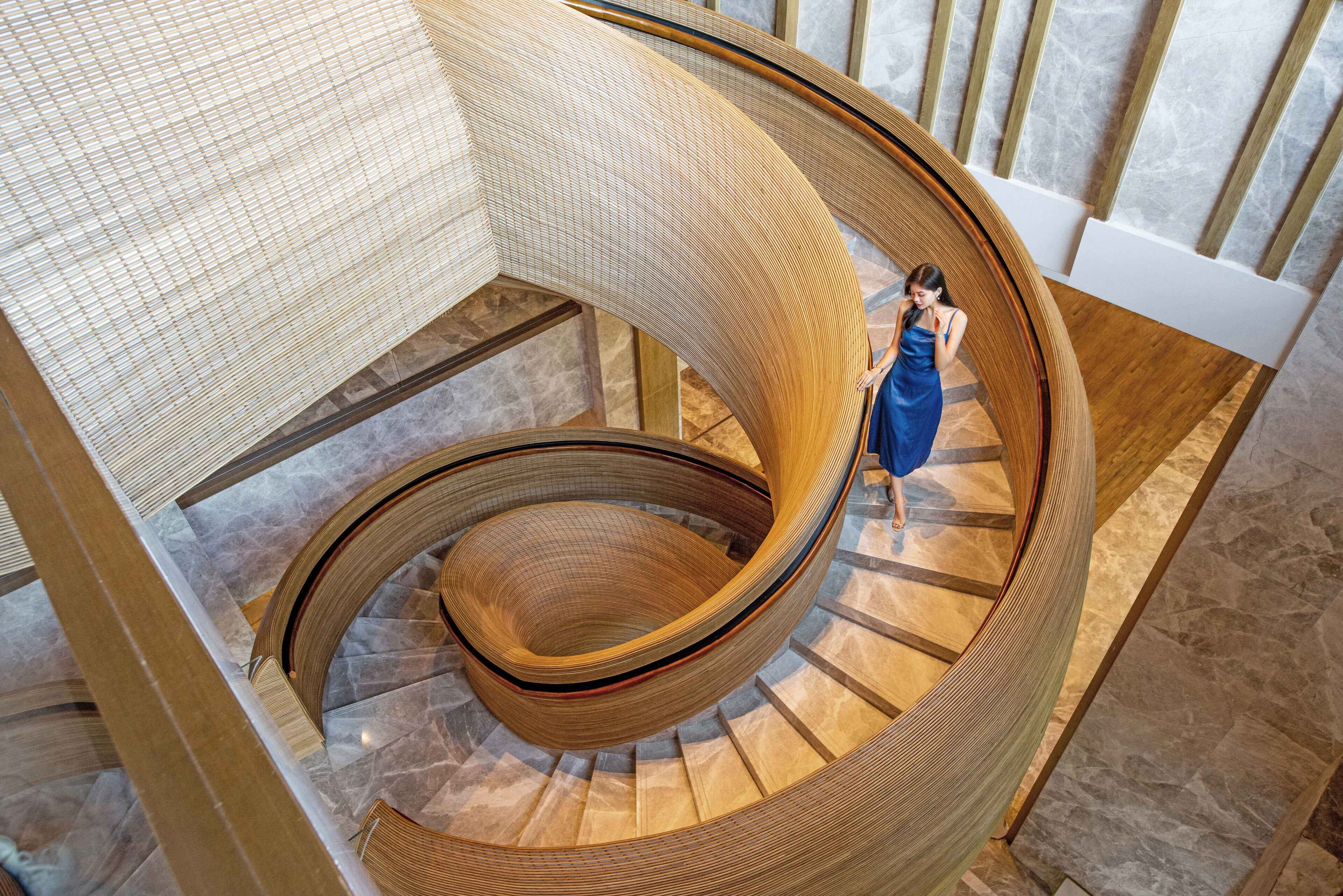 A spiral staircase with a wooden finish and a person in a blue dress standing on the steps.