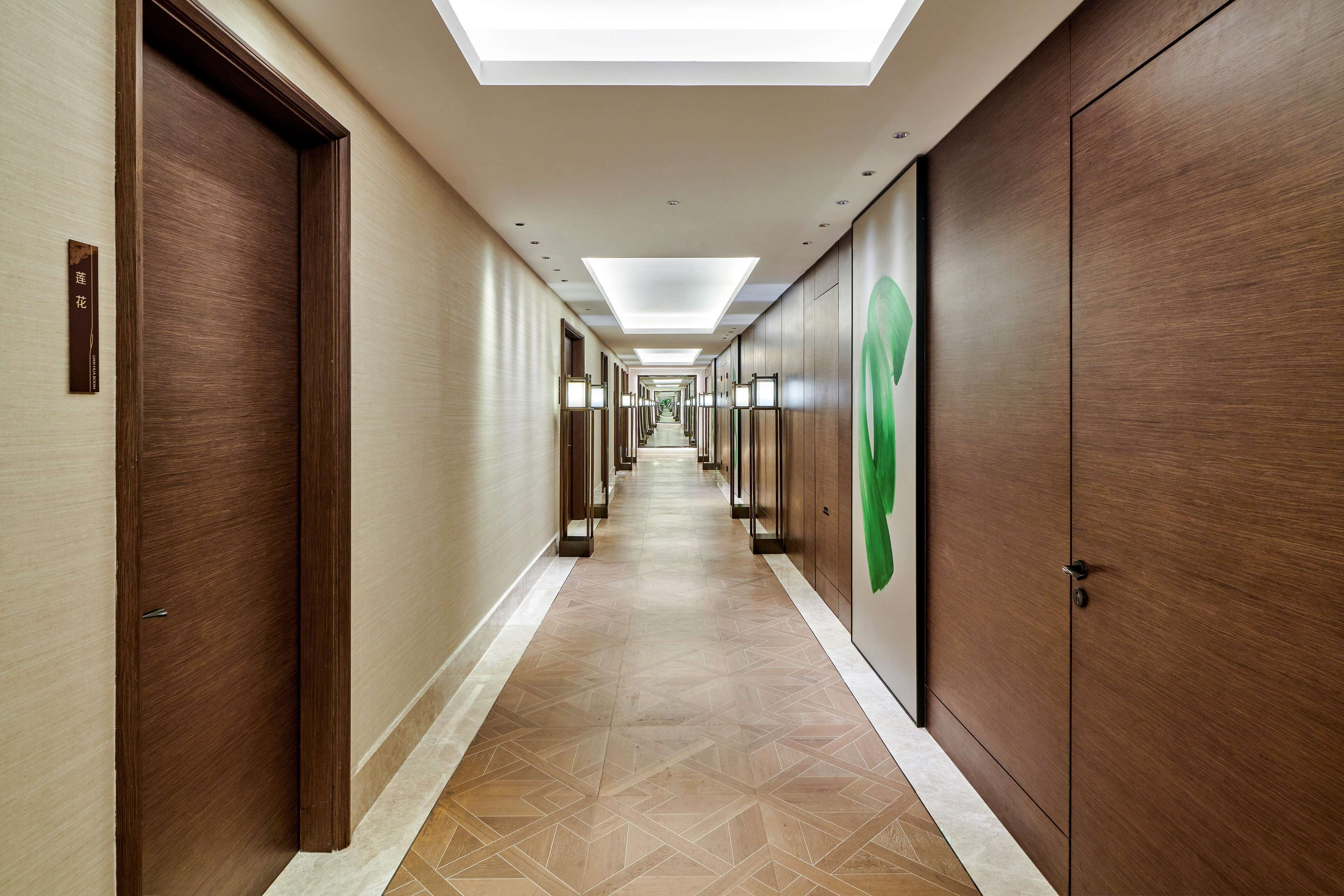 A hotel hallway with a geometric patterned floor, wooden doors, and a green logo on the wall.