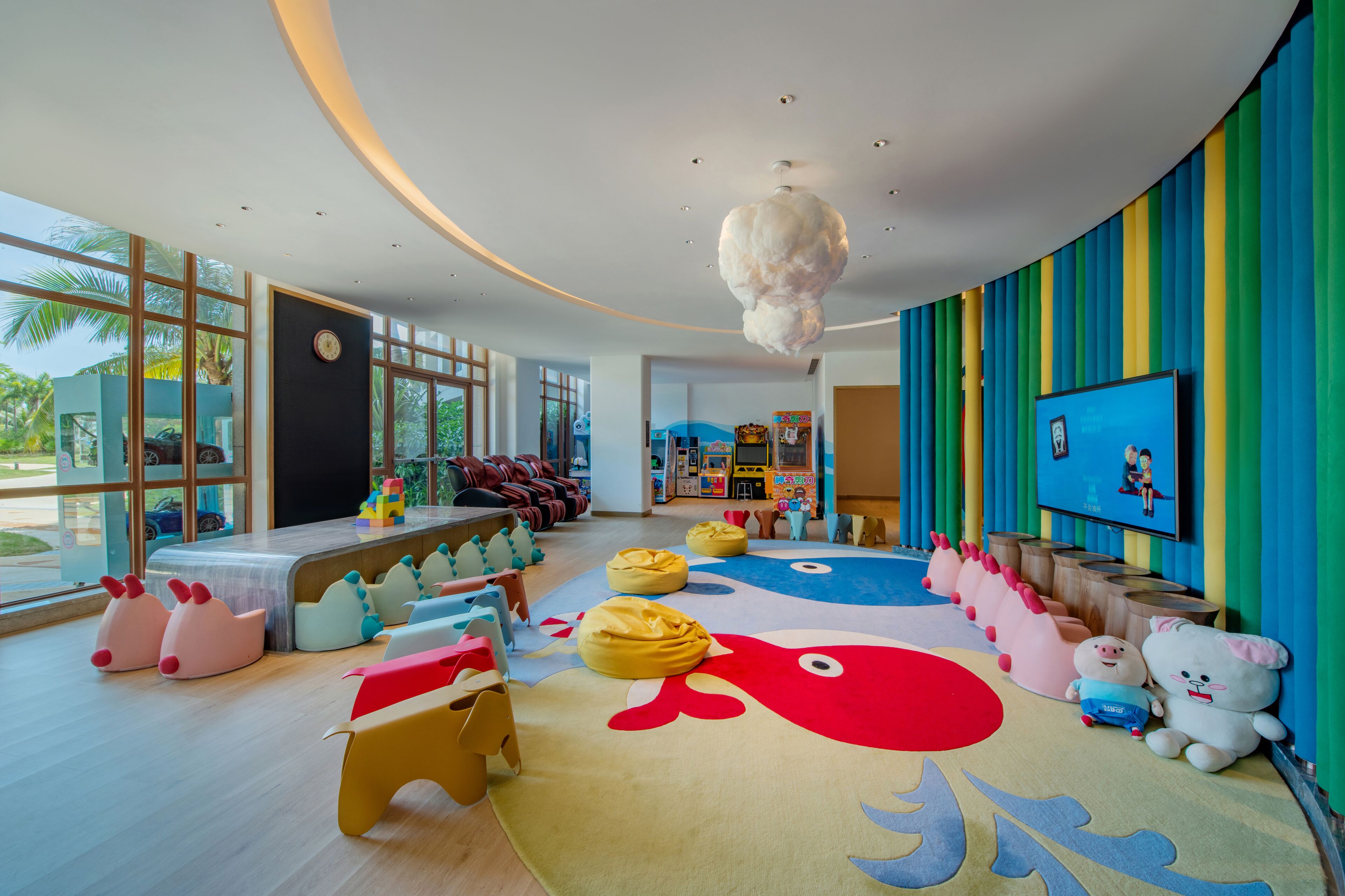 A brightly colored children's play area with bean bags, a large rug with a whale design, and a TV on the wall.