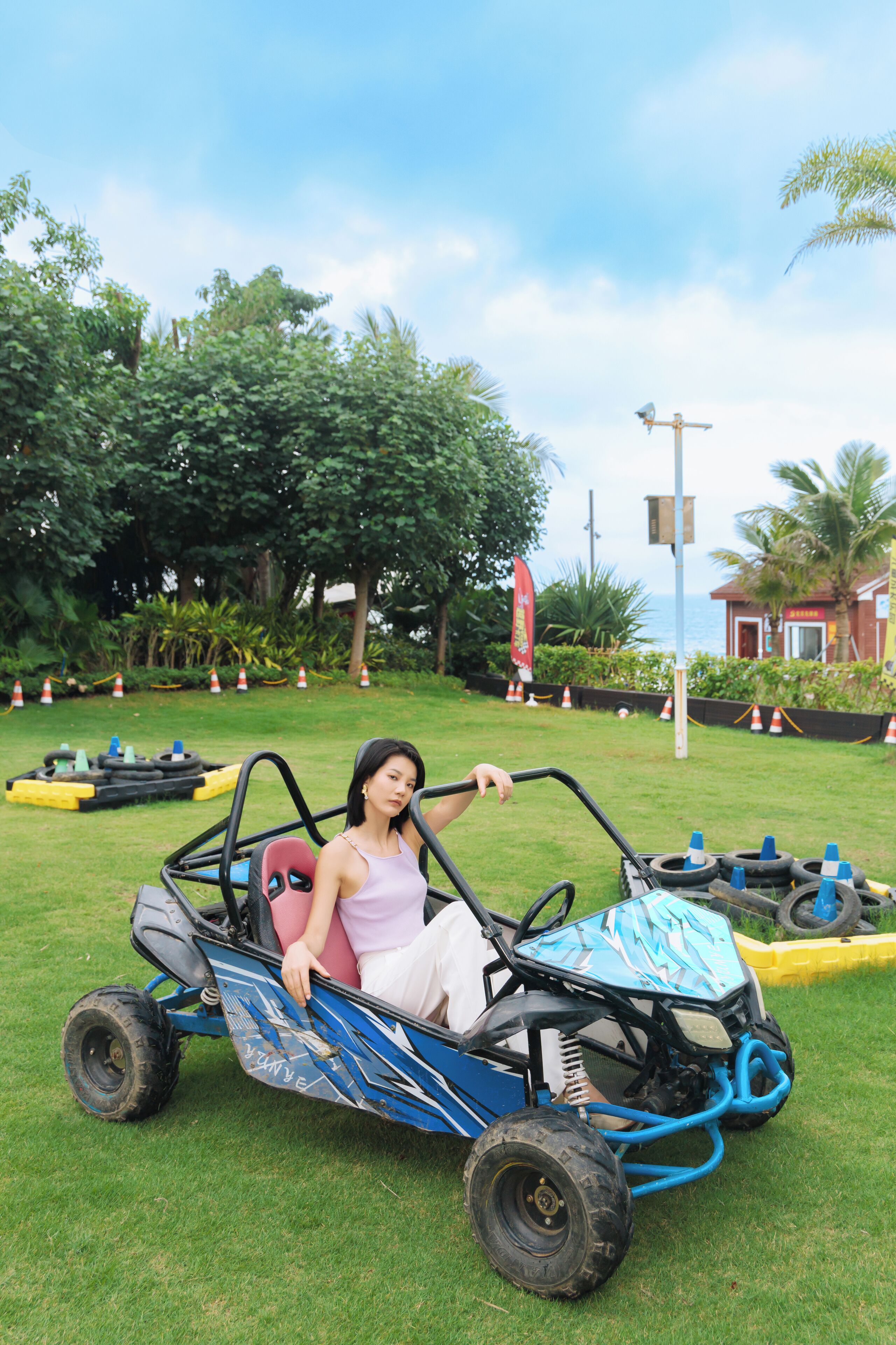 A person in a blue and black go-kart on a grassy area with trees and a building in the background.