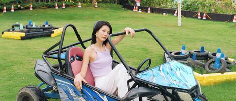 A person in a blue and black go-kart on a grassy area with trees and a building in the background.