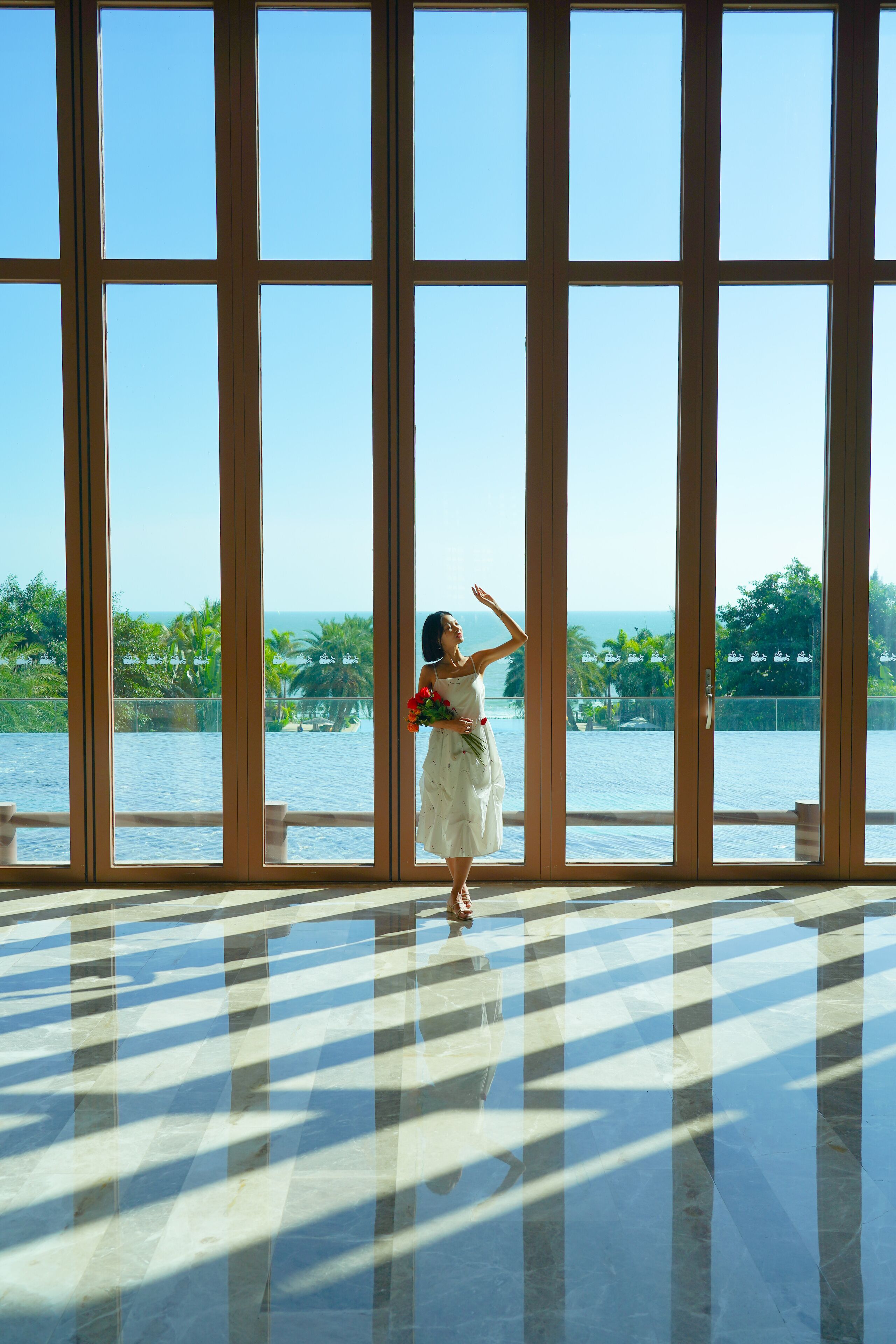 A room with large windows, a checkered floor, and a view of the ocean and greenery.
