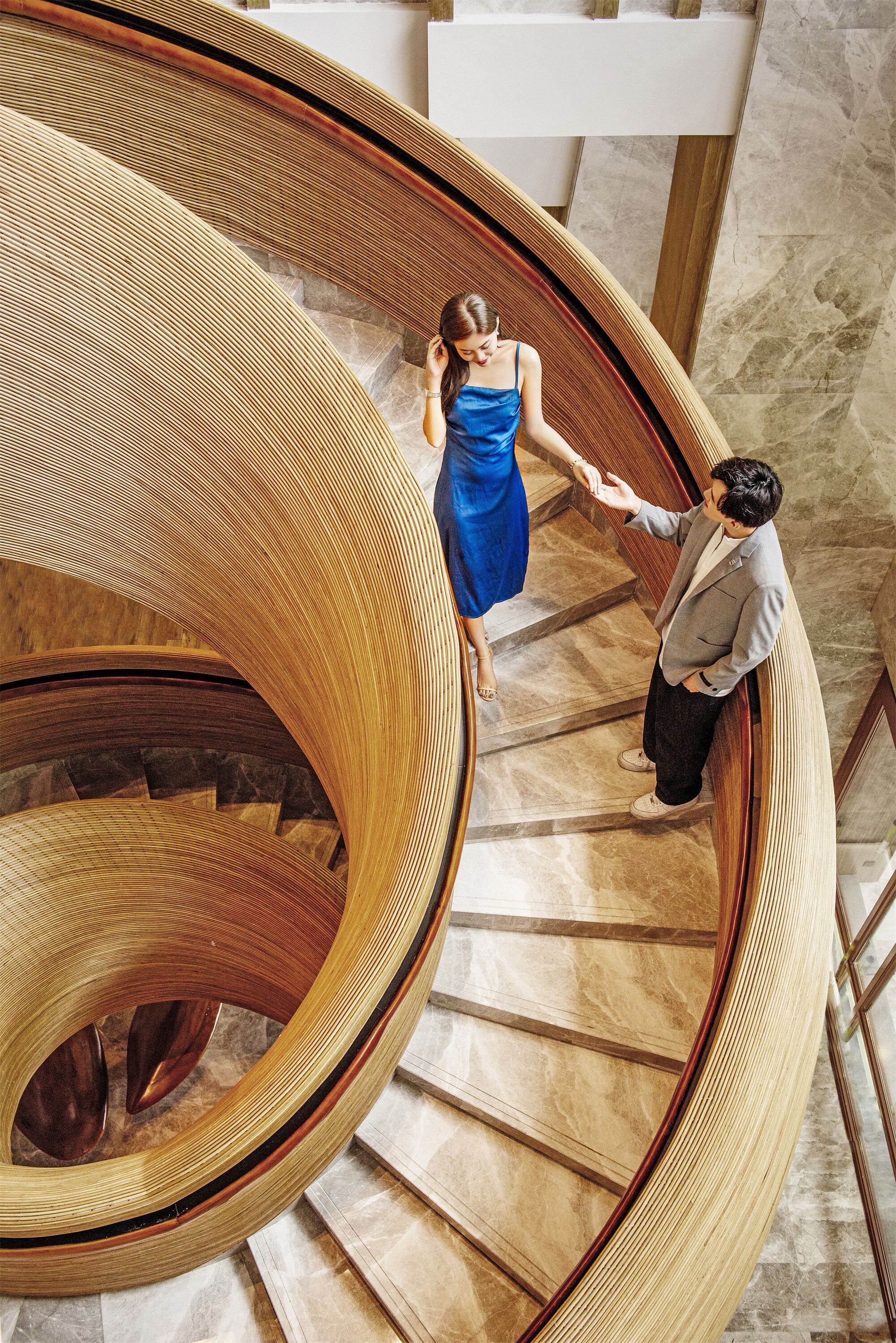 A spiral staircase with a wooden design, marble steps, and a handrail.