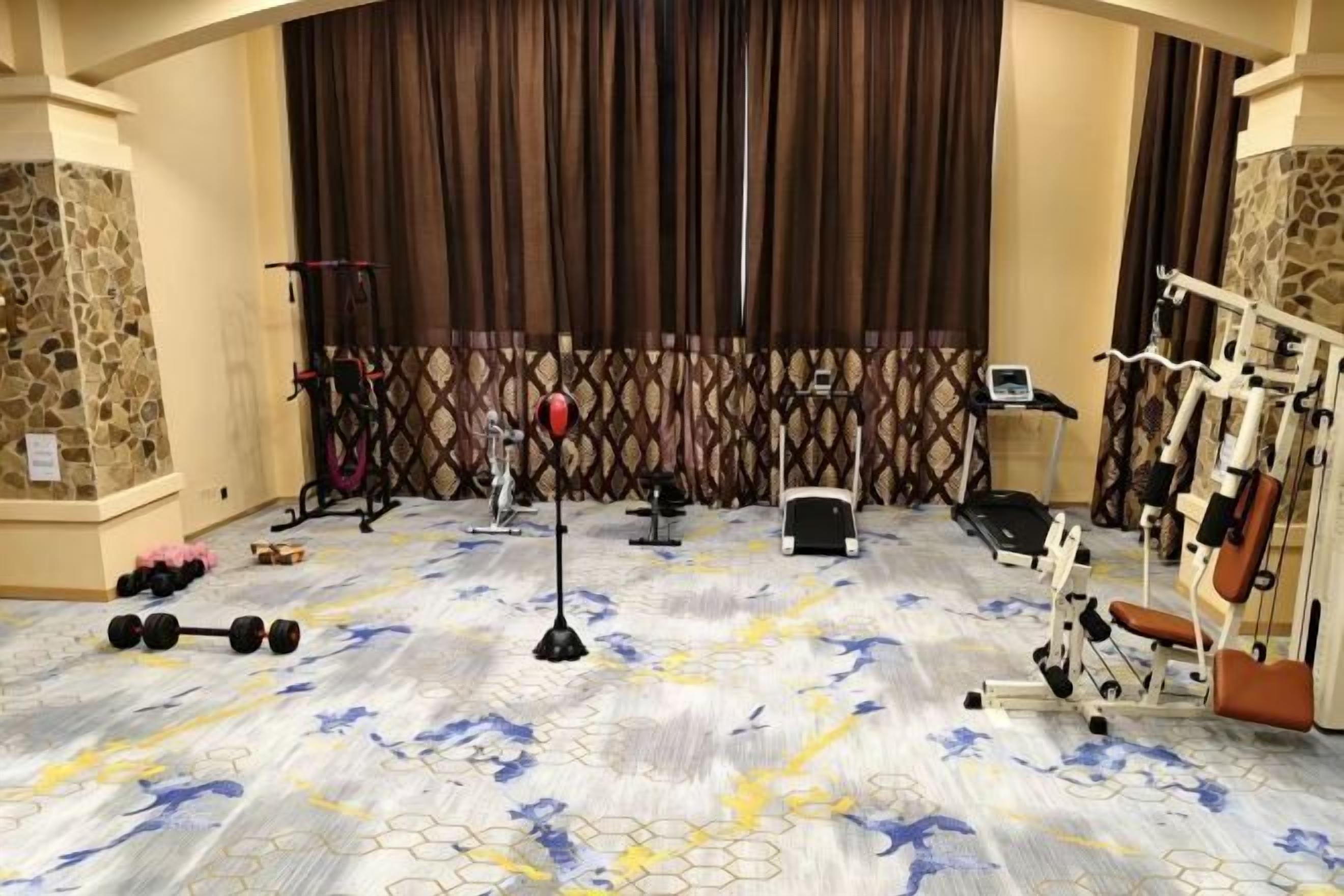 A gym with exercise equipment, a patterned carpet, and a stone wall.