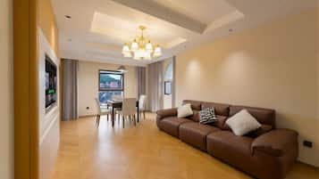 A modern living room with a brown leather sofa, a chandelier, and a dining area with a table and chairs.