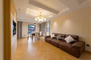 Una sala de estar moderna con un sofá de cuero marrón, una araña y una zona de comedor con mesa y sillas.