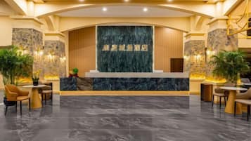 Zona de recepción de un hotel con mostrador de mármol, asientos y plantas.