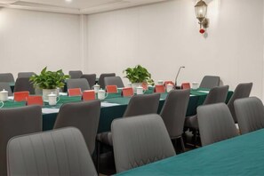 Un salón de conferencias con una larga mesa, sillas, tarjetas de identificación y plantas en macetas.