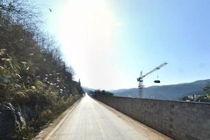 A road with a construction crane on the right, surrounded by vegetation and hills in the distance. - Taimei Holiday Hotel (Chongqing)