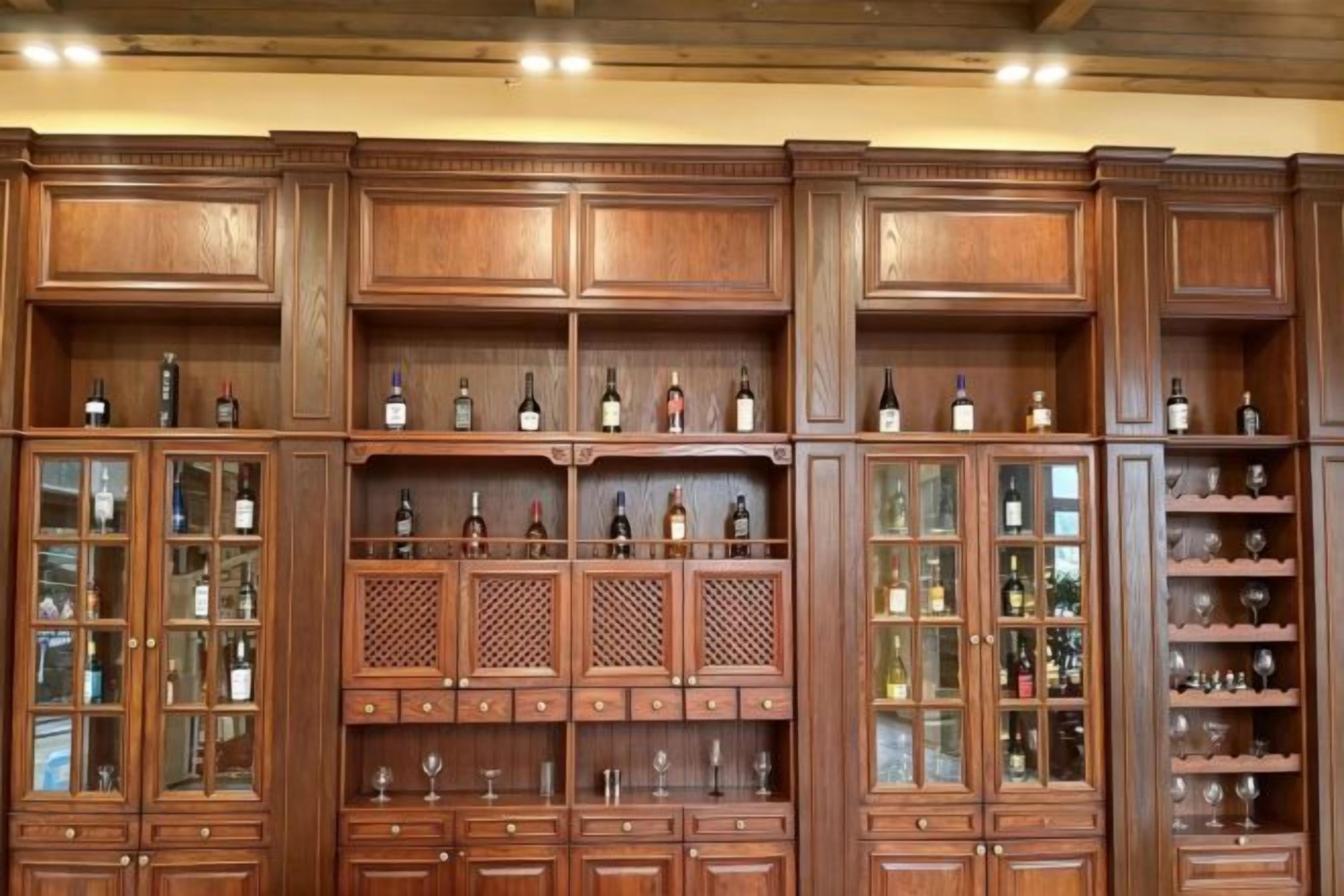 A large wooden wine cabinet with multiple shelves and glass doors, containing various bottles and glasses.