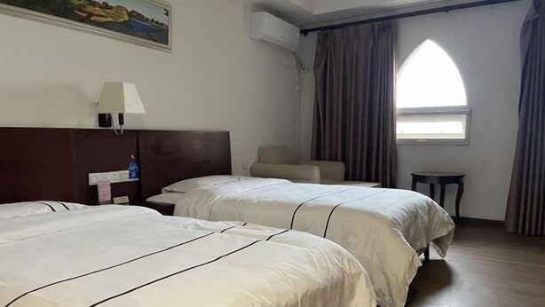 A hotel room with two beds, a chair, a small table, a painting on the wall, and a window with curtains. - Taimei Holiday Hotel (Chongqing)