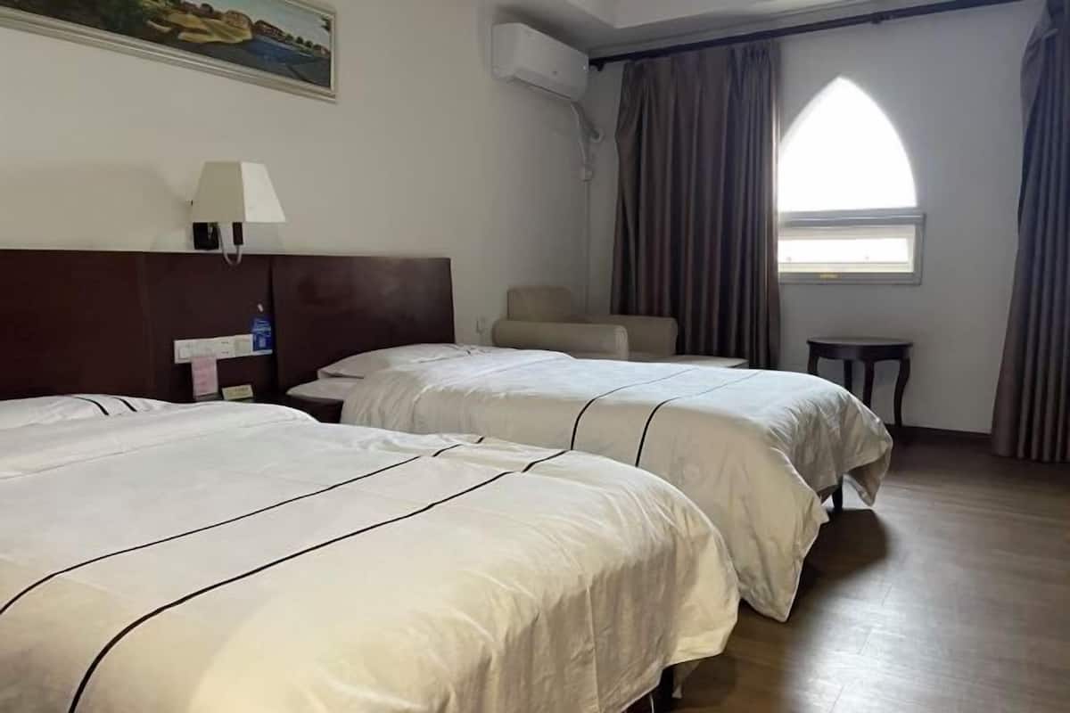 A hotel room with two beds, a chair, a small table, a painting on the wall, and a window with curtains.