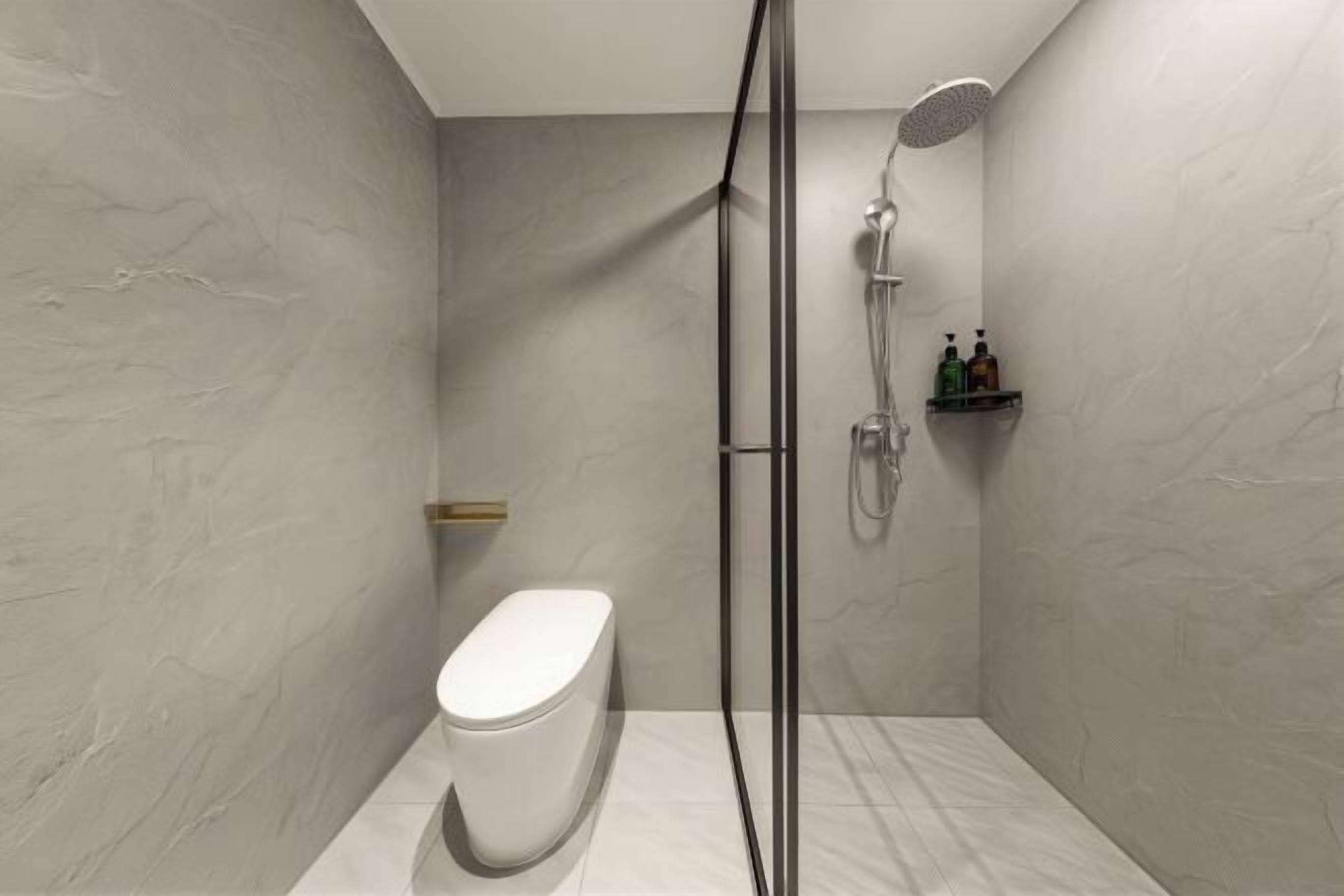A modern bathroom with a toilet, shower, and a shelf with toiletries.