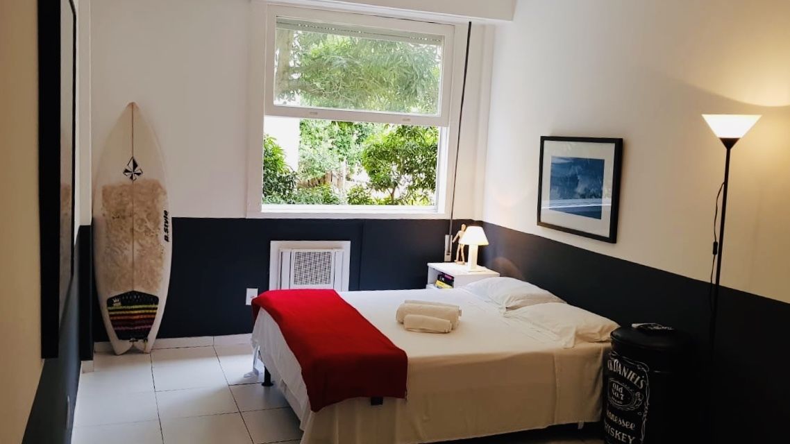 Una camera da letto con un letto, una finestra, un'asse da surf, una lampada e un quadro appeso al muro.