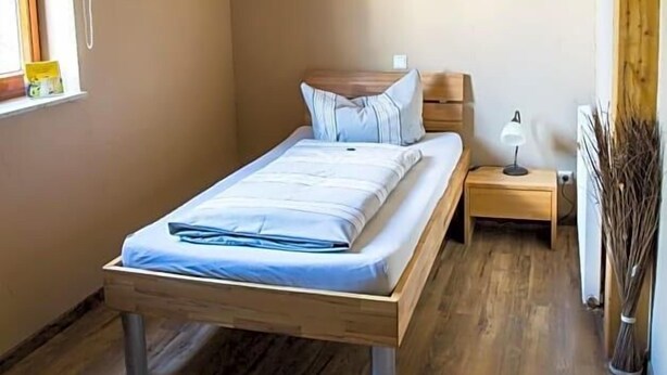Ein Schlafzimmer mit einem hölzernen Bett, einem Nachttisch, einer Lampe und einem Fenster.