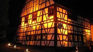 Ein traditionelles Fachwerkhäuschen mit einem steilen Walmdach, erleuchteten Fenstern und einem sichtbaren Schild.