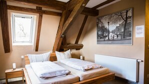 Un dormitorio con techo inclinado, una cama de madera, una mesita de noche, un ventanal y una pintura de paisaje urbano.
