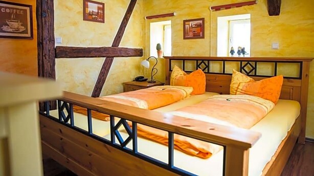Una cama doble con cabecera y piecera de madera, dos mesitas de noche y una ventana con vistas.