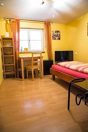 A room with a bed, a desk, a chair, a TV, and a window with curtains.