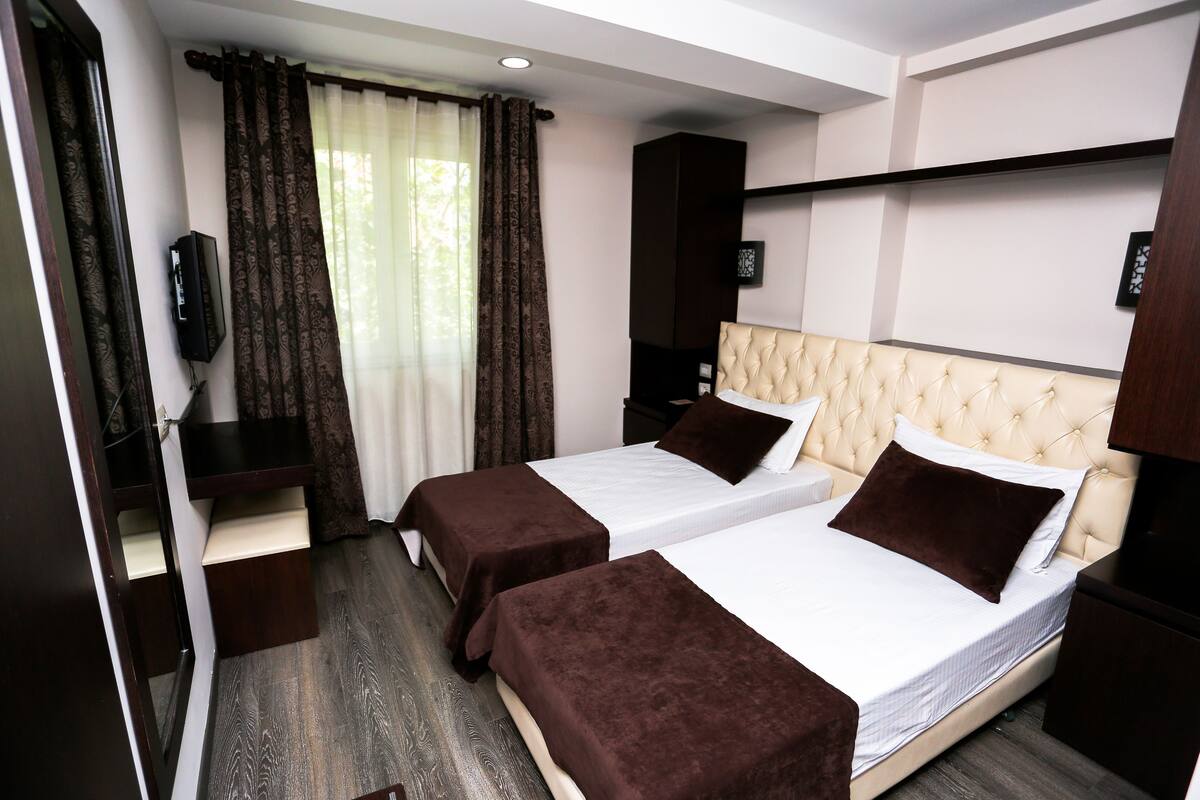 A hotel room with two beds, a TV, a wardrobe, and a window with curtains.