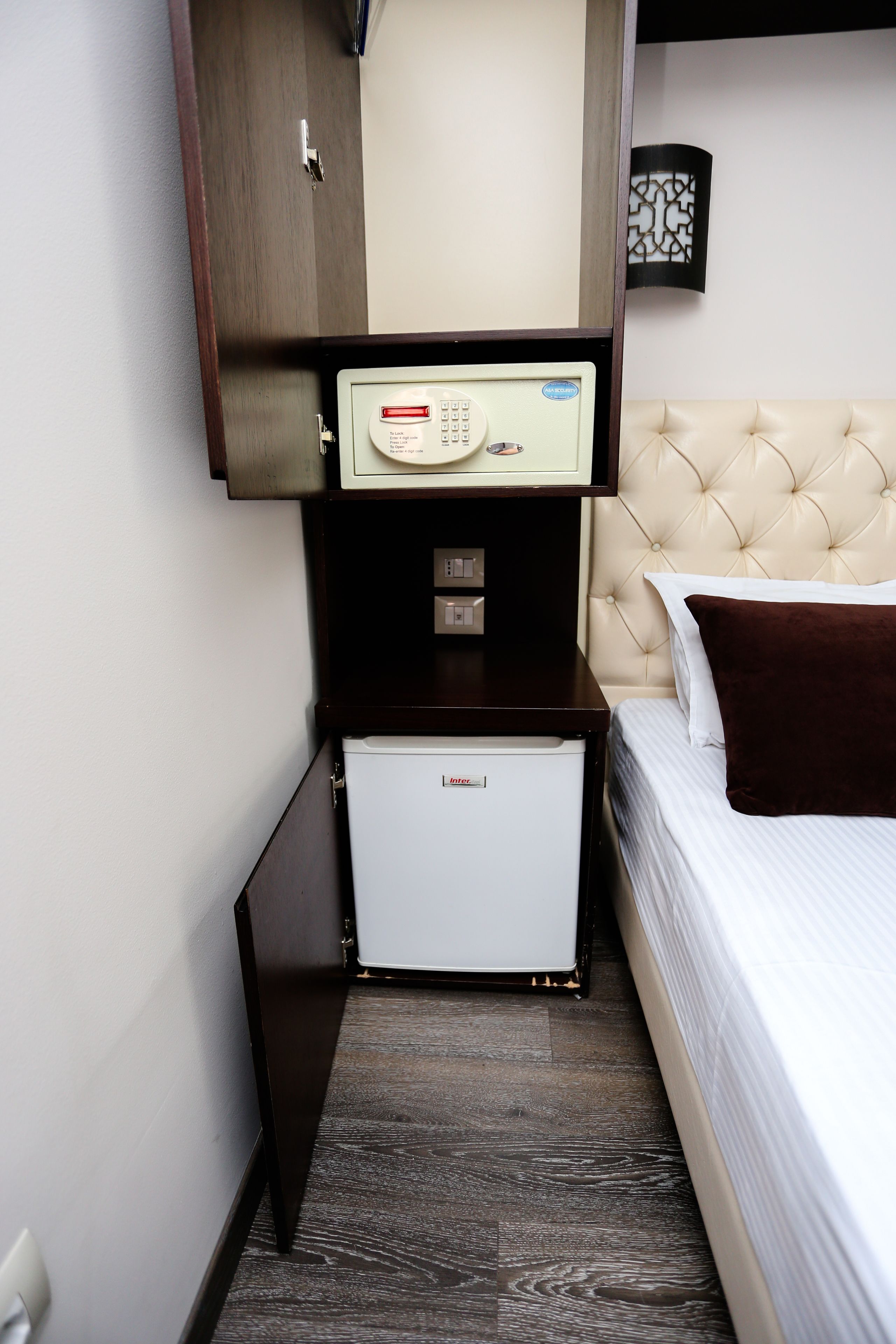 Une chambre d’hôtel compacte comprenant un lit, un mini-bar, un petit réfrigérateur et une armoire en bois.