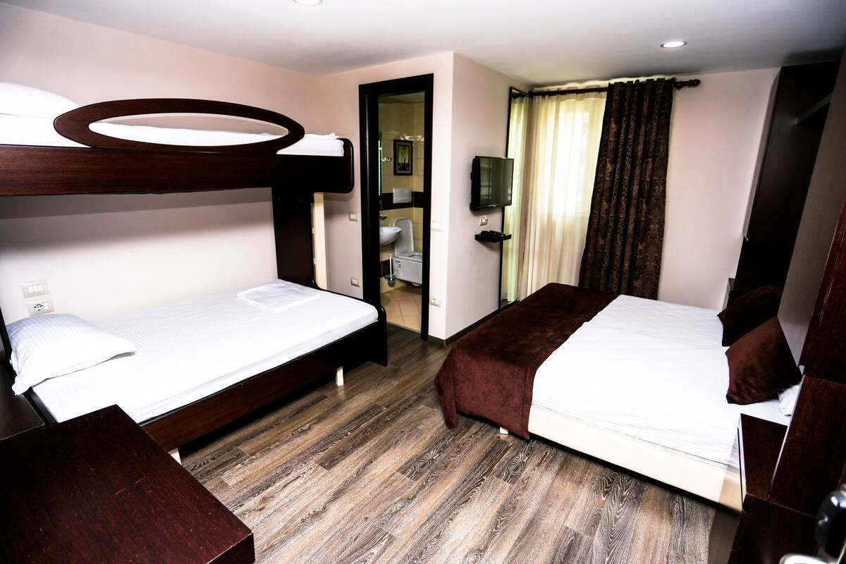 A hotel room with two beds, a wooden floor, a mirror, and a television.