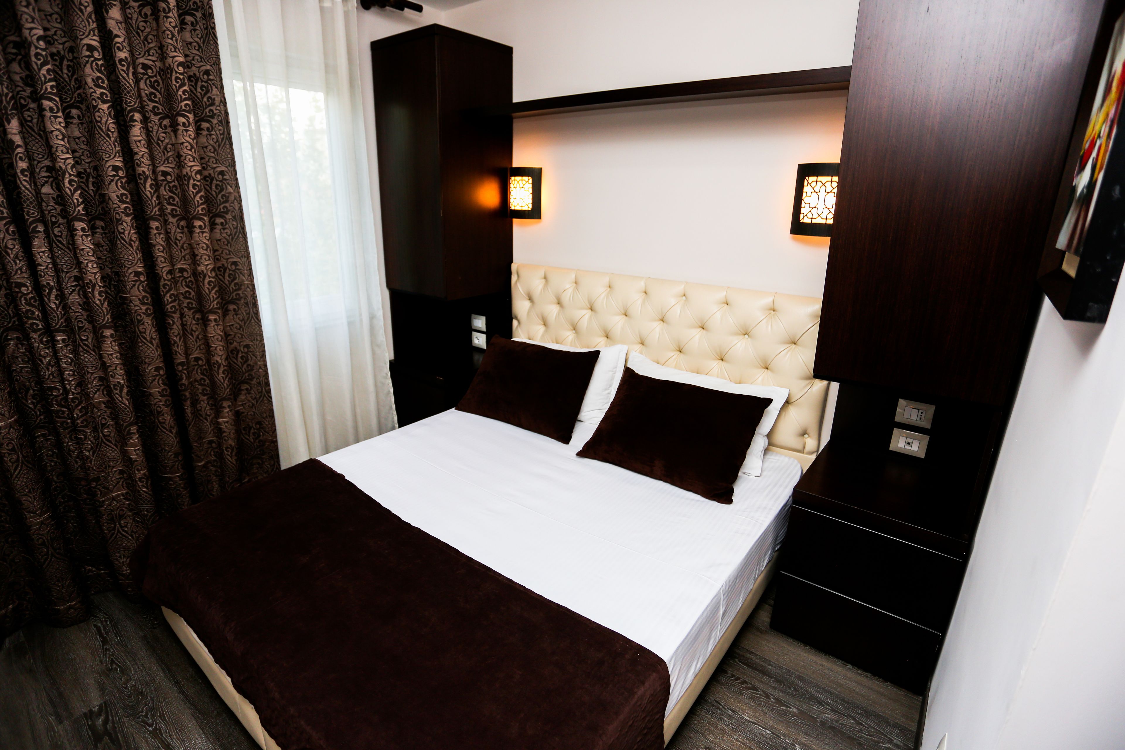 A neatly made bed with a white and brown bedspread, a tufted headboard, and two bedside lamps.