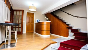 Uma sala de estar ampla, com escada de madeira, mesa de jantar e um banco estofado.