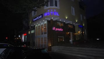 Un hotel con un letrero de neón, una entrada visible y un restaurante cercano.