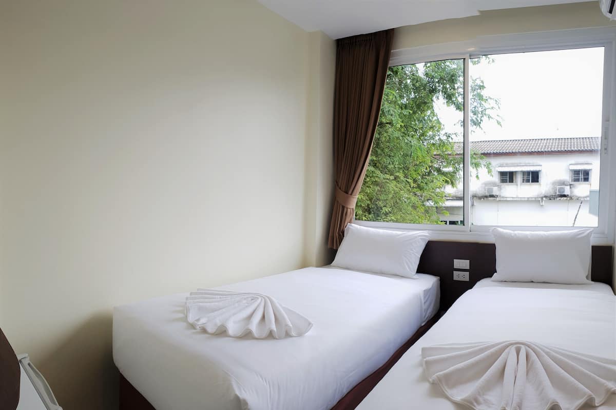 A hotel room with two beds, a window with curtains, and a view of buildings outside.