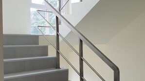 A modern staircase with metal railings and a view of the outdoors through a large window. - Top Hostel Samui (Koh Samui)